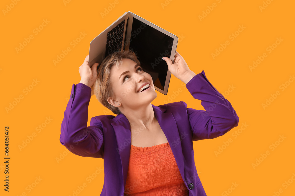 Happy young female programmer with laptop on yellow background