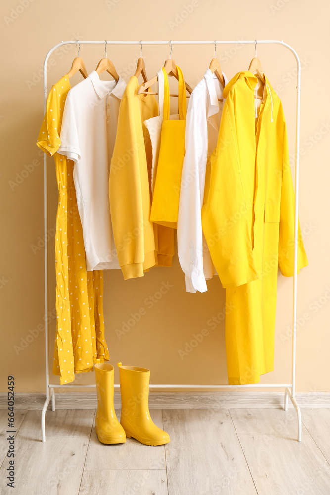 Rack with stylish clothes and rubber boots near color wall