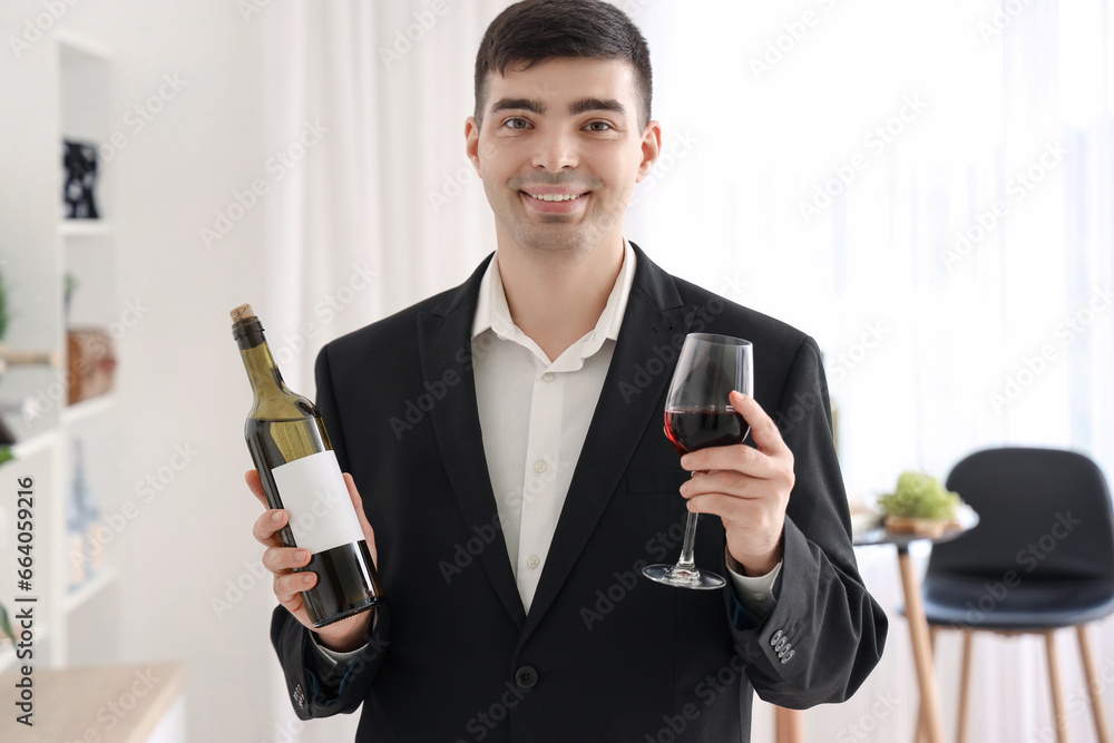 Young sommelier with bottle and glass of red wine in kitchen