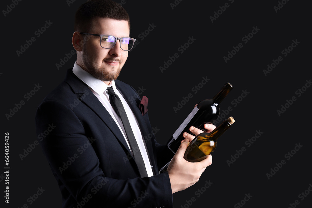 Young sommelier holding bottles with different types of wine on black background