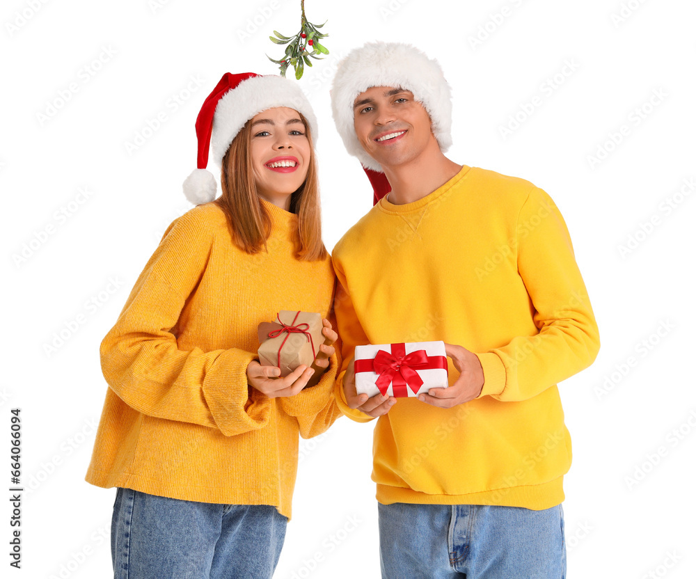 Young couple with Christmas gifts under mistletoe branch on white background