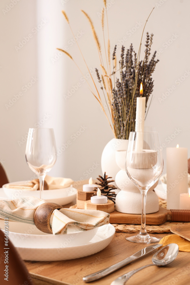 Elegant table setting with dried flowers, burning candles and pine cones