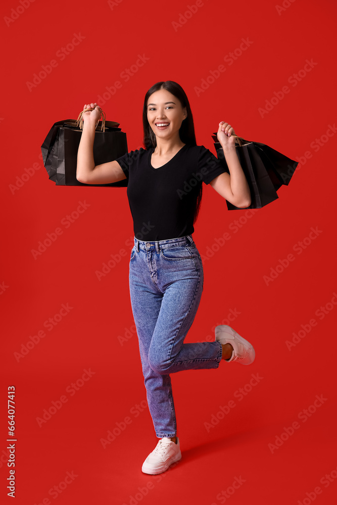 Beautiful young Asian woman with shopping bags on red background. Black Friday sale