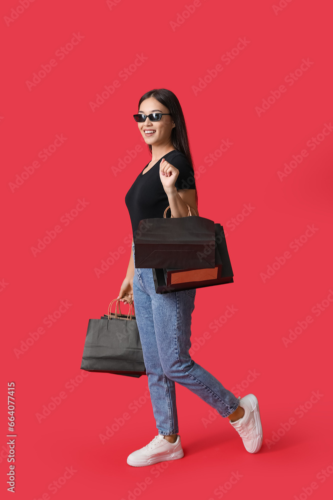 Beautiful young Asian woman with shopping bags on red background. Black Friday sale