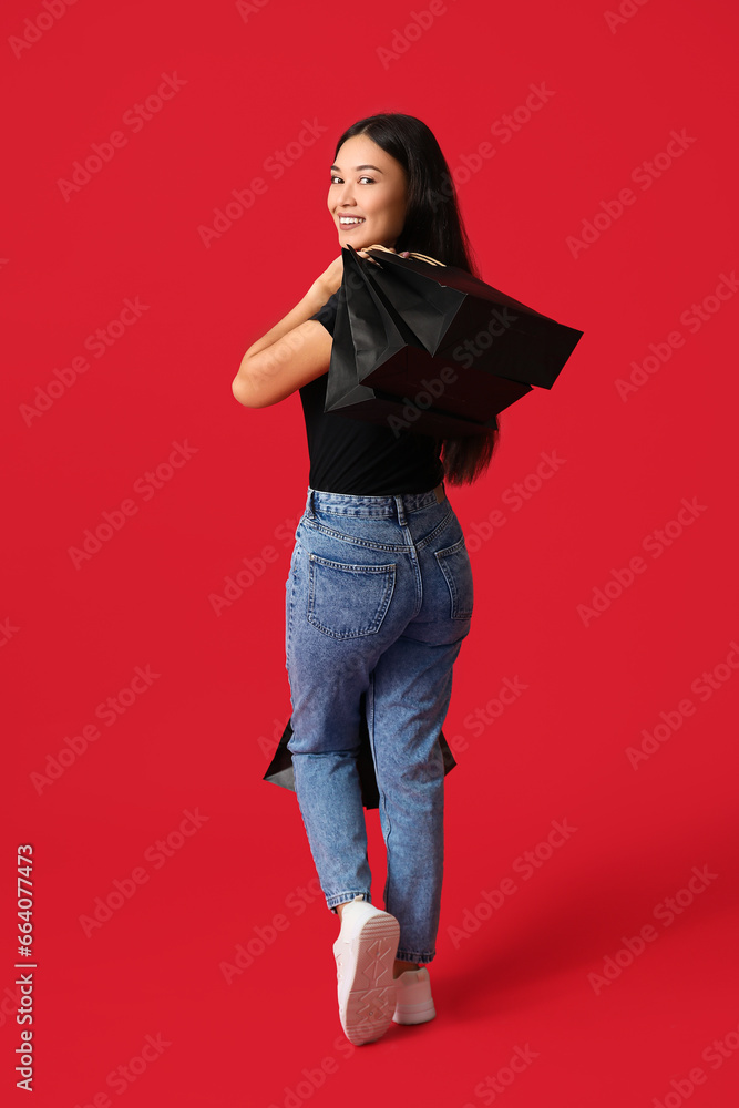 Beautiful young Asian woman with shopping bags on red background. Black Friday sale