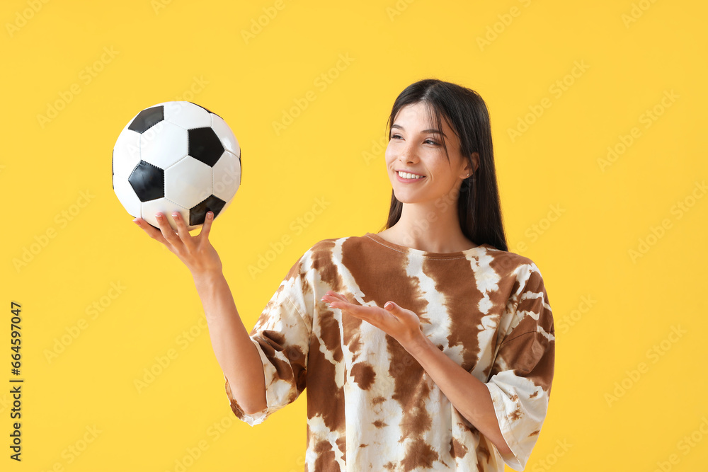 Young woman with soccer ball on yellow background