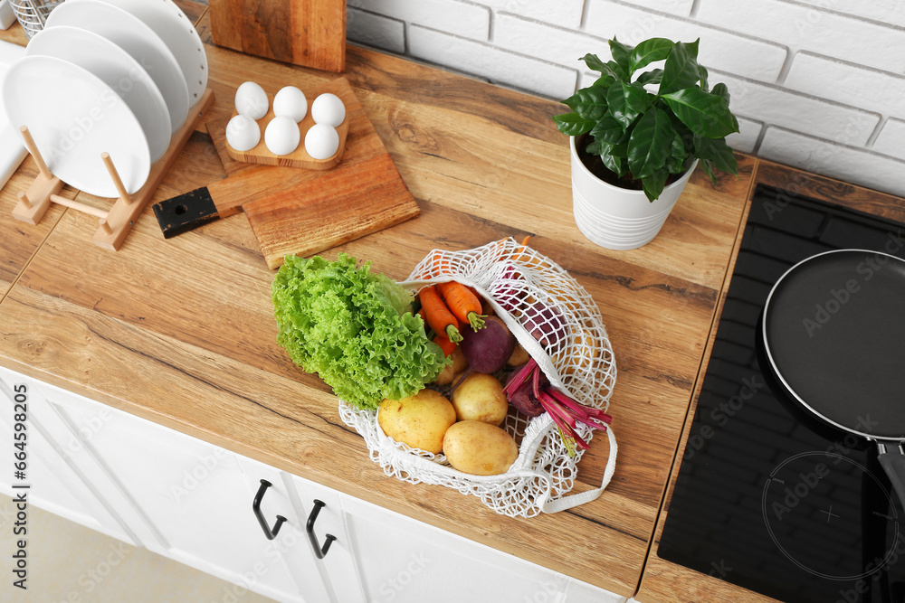 Mesh bag with different fresh vegetables on counter in kitchen