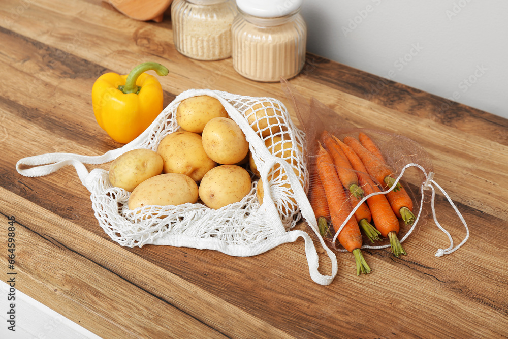 Mesh bags with different fresh vegetables on counter in kitchen, closeup