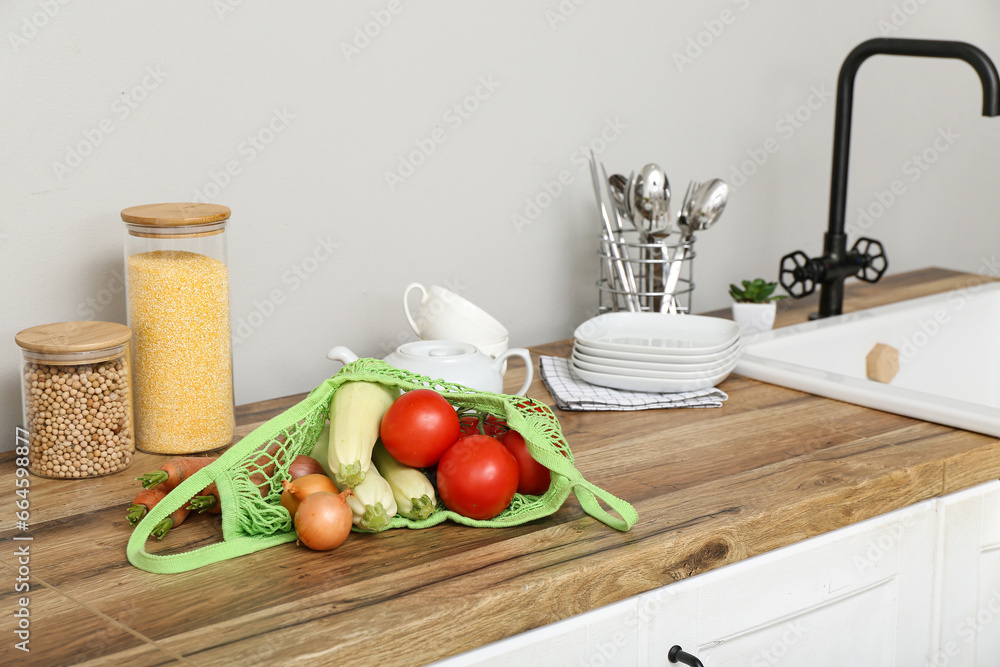 Mesh bag with different fresh vegetables on counter in kitchen