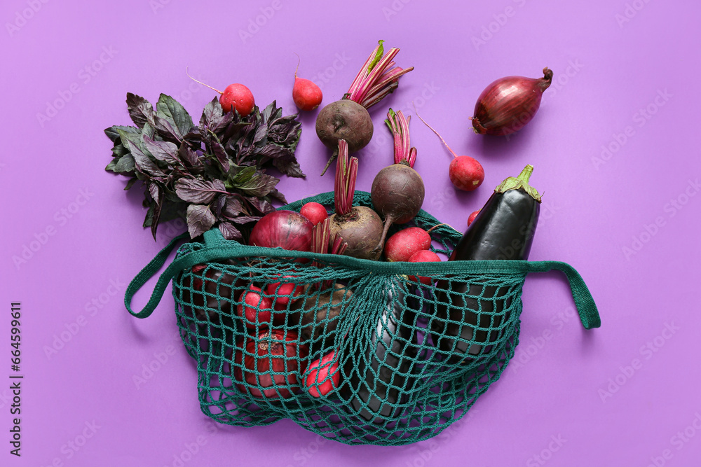 Mesh bag with different fresh vegetables on purple background