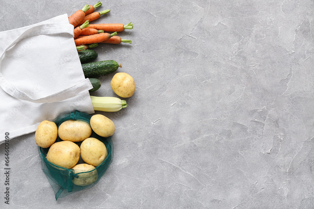 Eco bags with different fresh vegetables on grey background