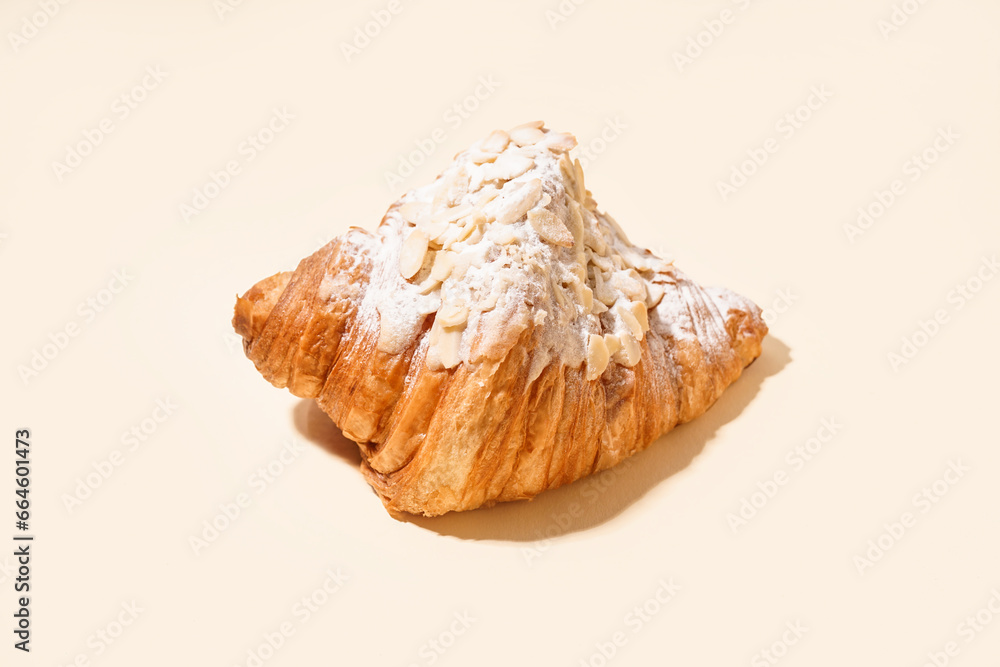 Sweet croissant with powdered sugar and nuts on beige background