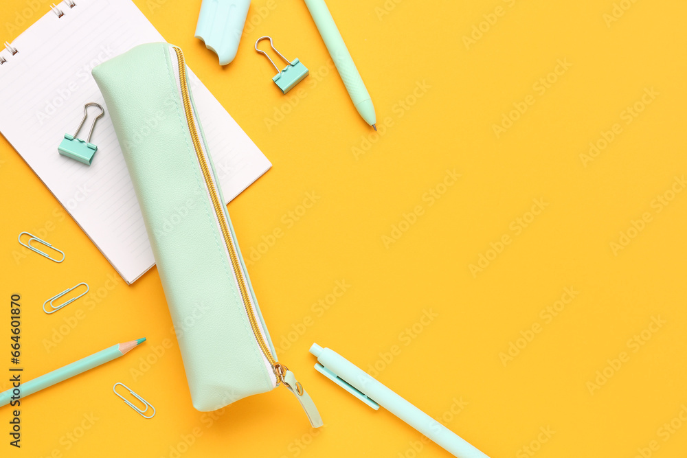 Pencil case with different stationery and notebook on orange background