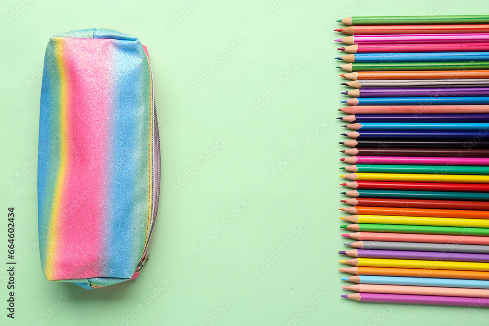 Pencil case with different colorful pencils on green background