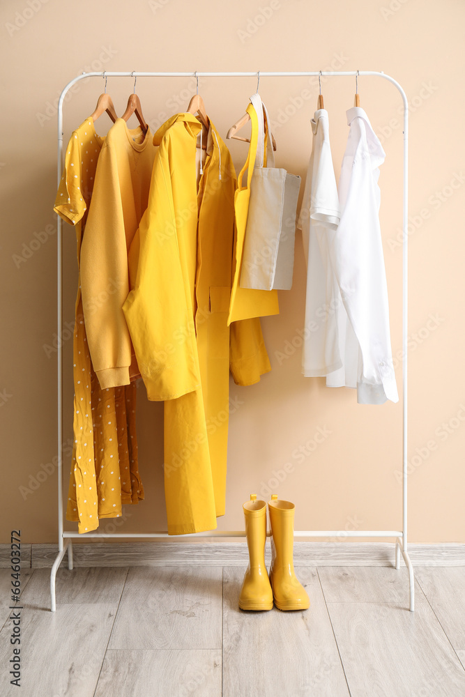 Rack with stylish clothes and rubber boots near color wall