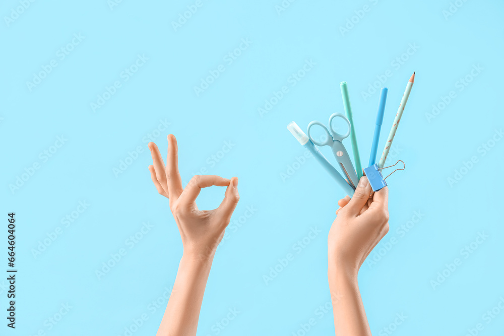 Hands with set of stationery showing OK gesture on light blue background