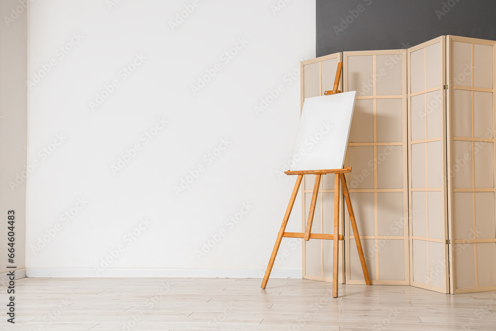 Wooden easel with blank canvas near white wall