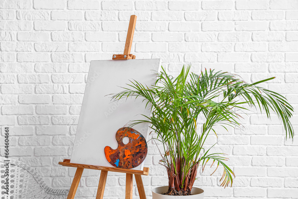 Wooden easel with blank canvas near white brick wall