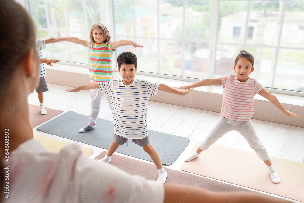 Group of little children practicing yoga with instructor in gym