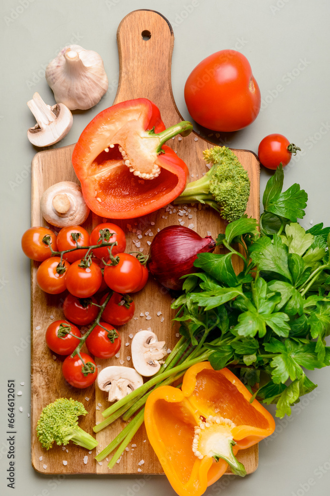 Wooden board with fresh vegetables and greenery on grey background