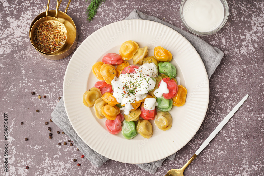 Plate of boiled colorful dumplings with sour cream and dill on dark background