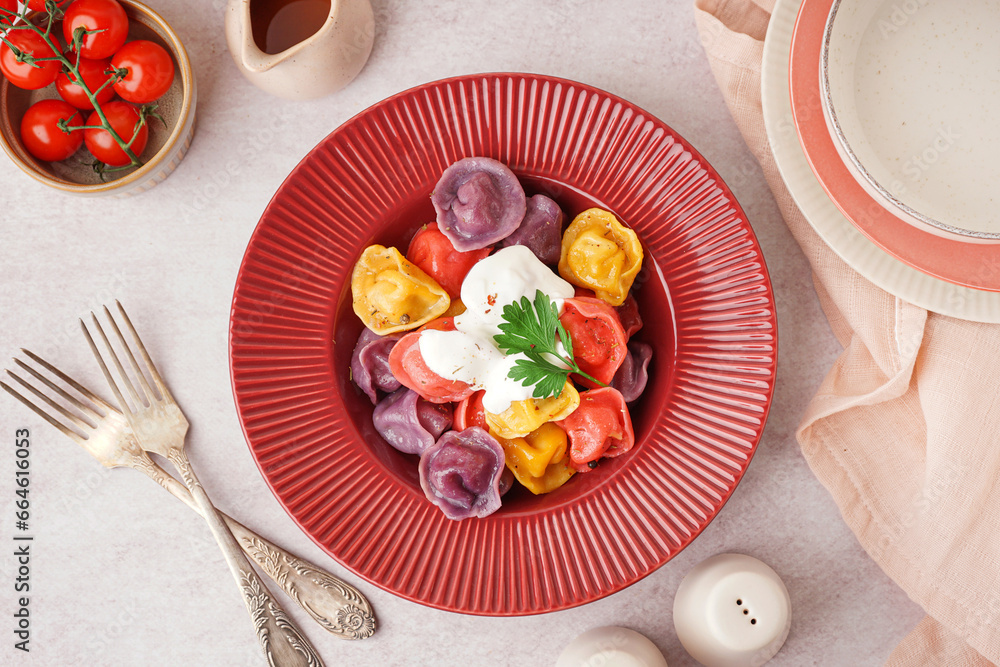 Plate of boiled colorful dumplings with sour cream and parsley on white background