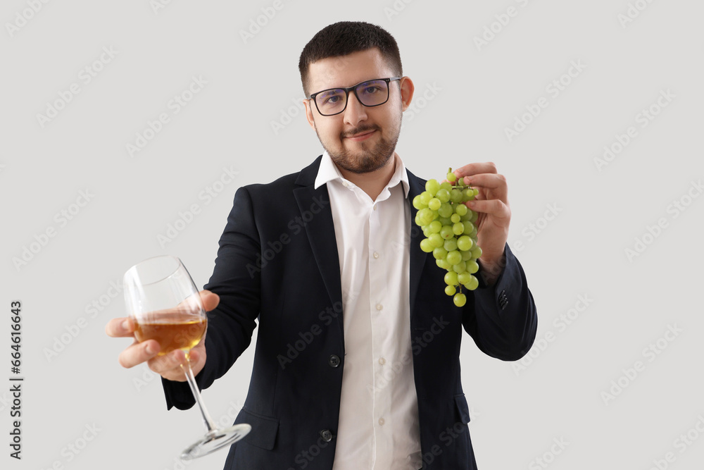 Young sommelier with glass of wine and grapes on grey background