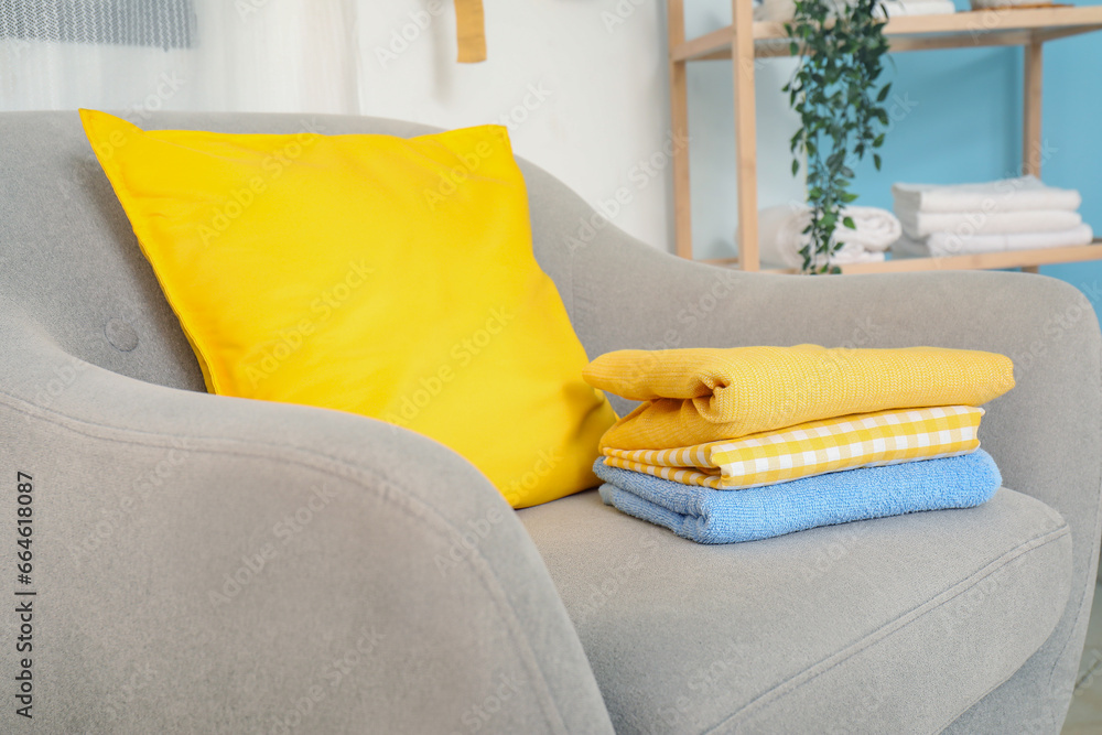 Stack of clean laundry and colorful pillow on armchair, closeup