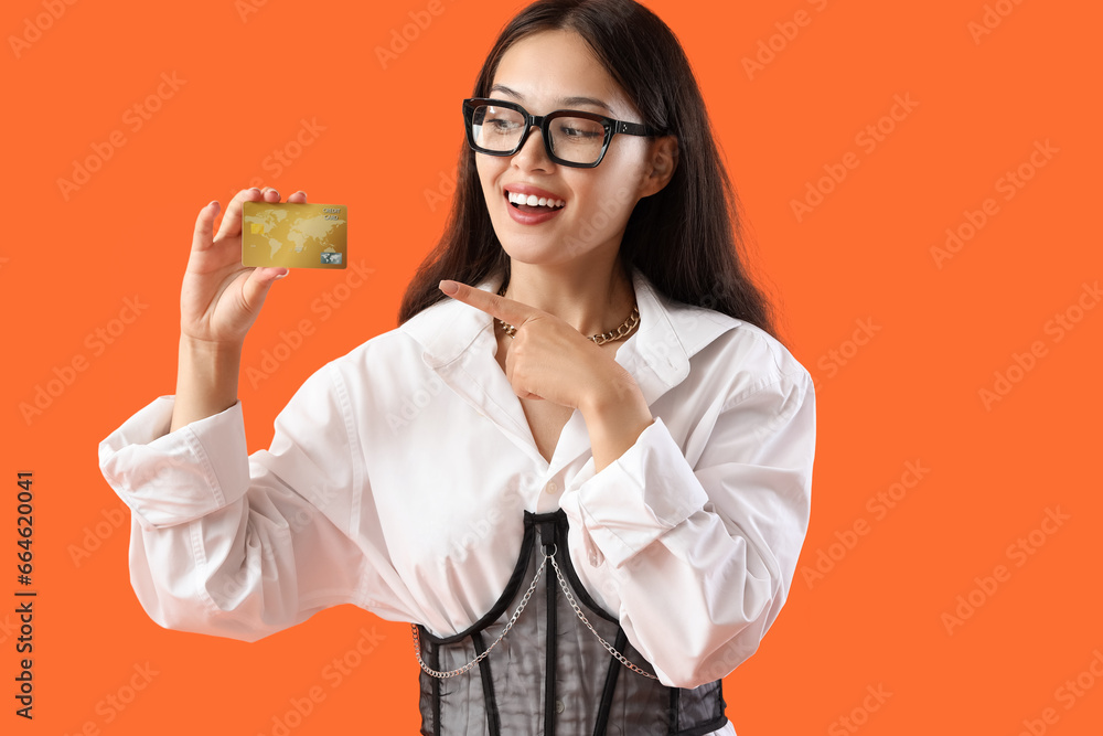 Young Asian woman pointing at credit card on orange background