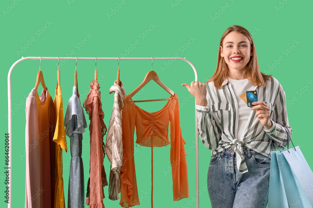 Young woman with credit cards and shopping bags pointing at clothes on green background