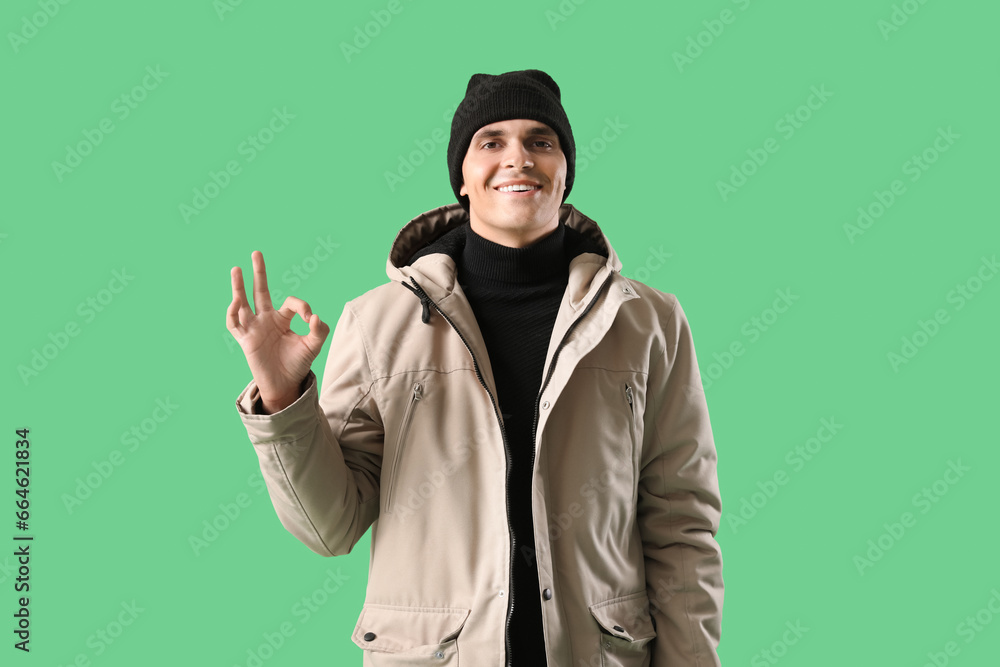 Young man in winter clothes showing OK on green background