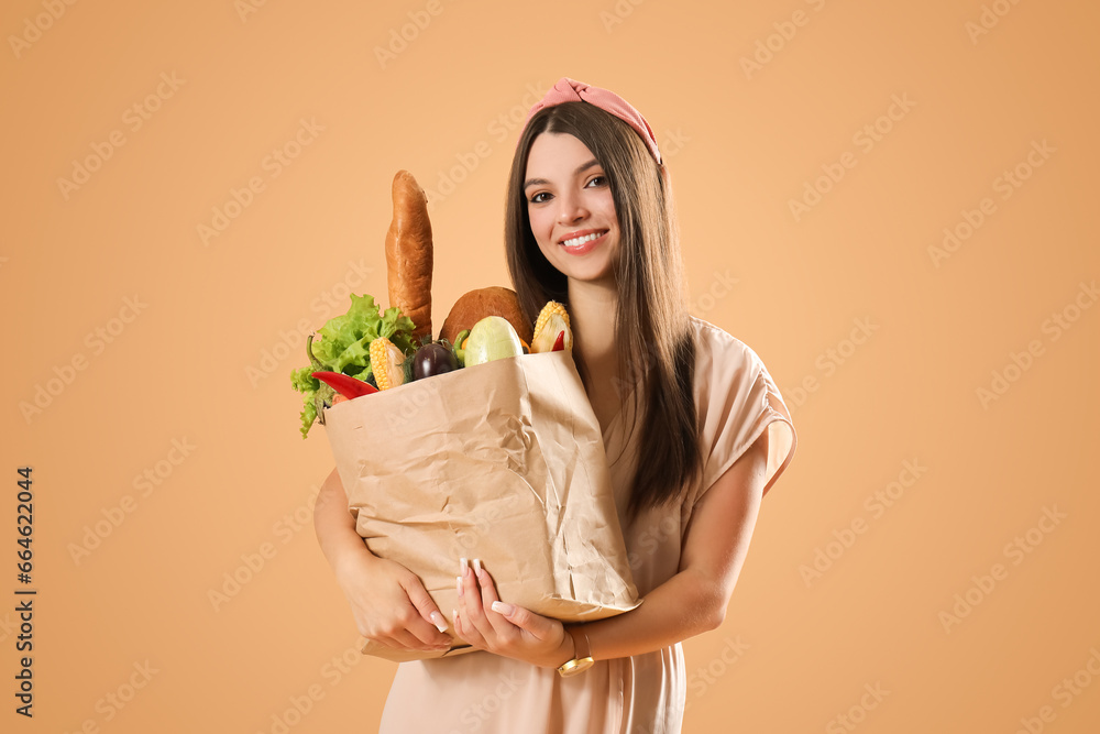 Young woman holding paper bag with fresh vegetables and fruits on brown background