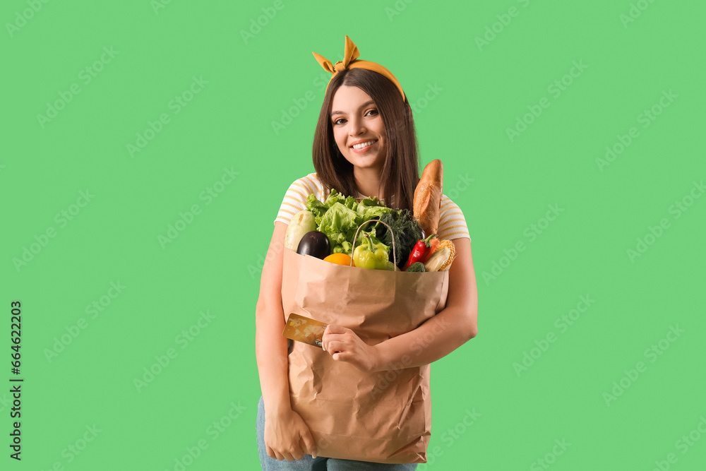 Young woman holding paper bag with fresh vegetables on green background