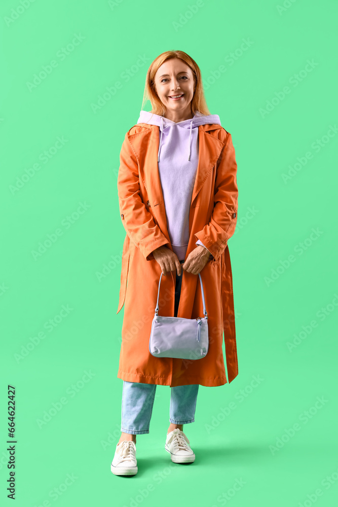 Mature woman in coat with bag on green background