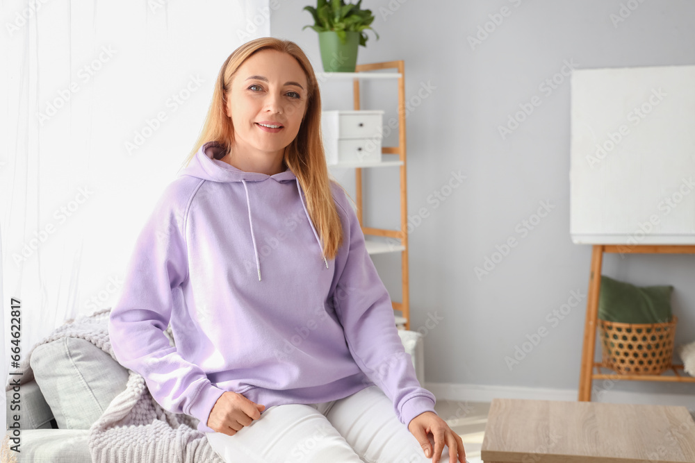 Mature woman in hoodie sitting on sofa at home