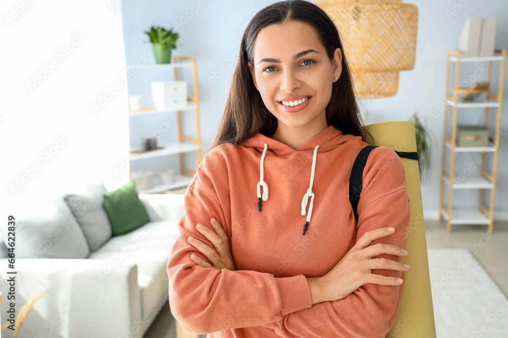 Young woman in hoodie with fitness mat at home