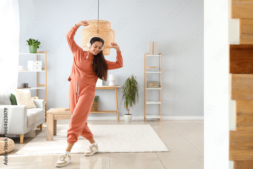 Young woman in hoodie with headphones dancing at home