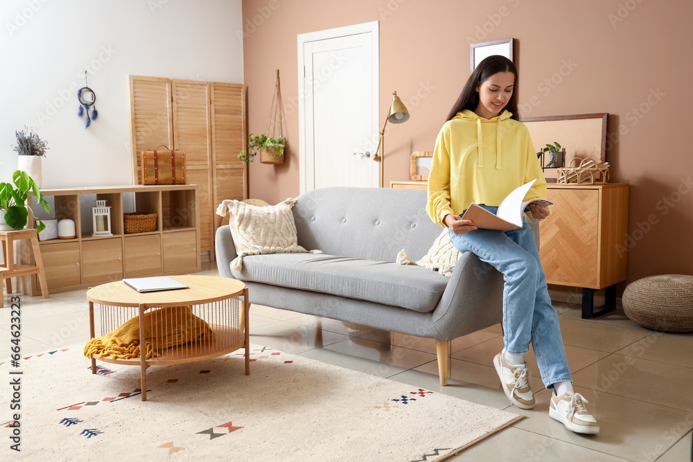 Young woman in hoodie reading magazine at home