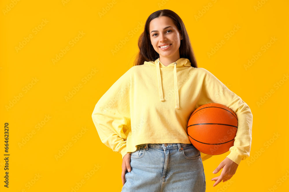 Young woman in hoodie with ball on yellow background