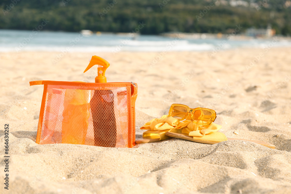 Cosmetic bag with bottles of sunscreen cream and flip flops on sand