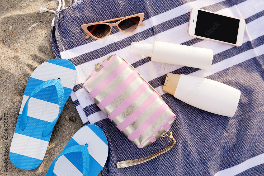 Cosmetic bag, bottles of sunscreen cream and flip flops on sandy background