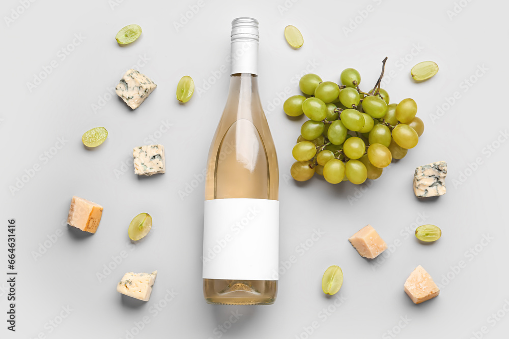 Bottle of tasty wine with blank label and grape on grey background