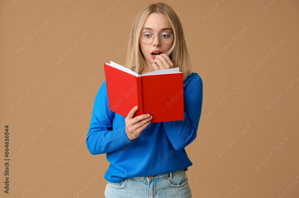 Beautiful young shocked woman with book on brown background