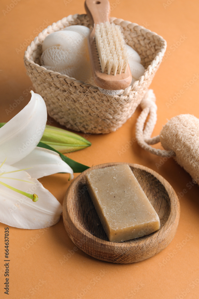 Bowl with soap bar, bath accessories and lily flowers on color background