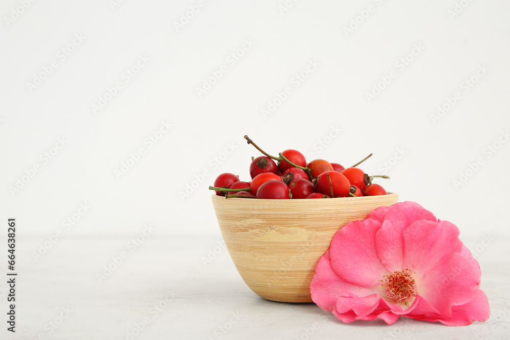 Bowl with fresh rose hip berries and flower on white background