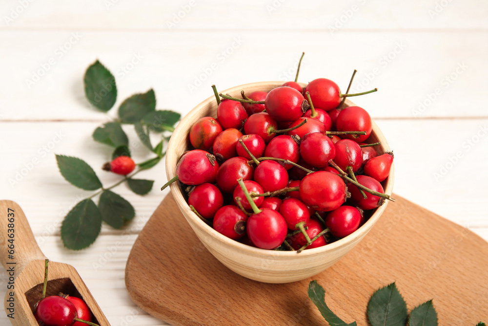 Bowl with fresh rose hip berries and leaves on white wooden background