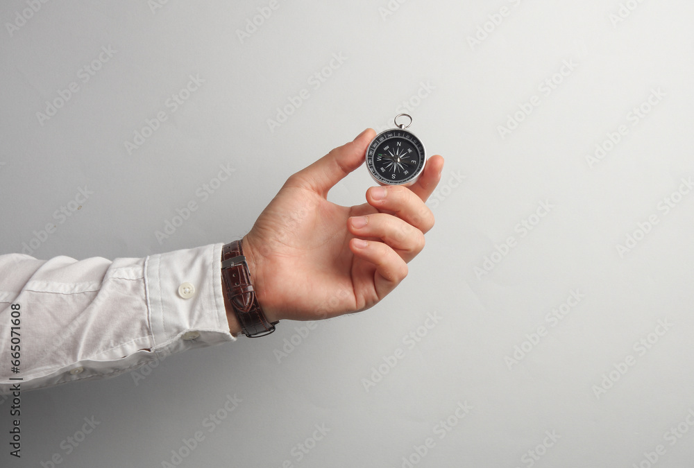 Mans hand in white shirt holds paper compass on gray background. Business concapt