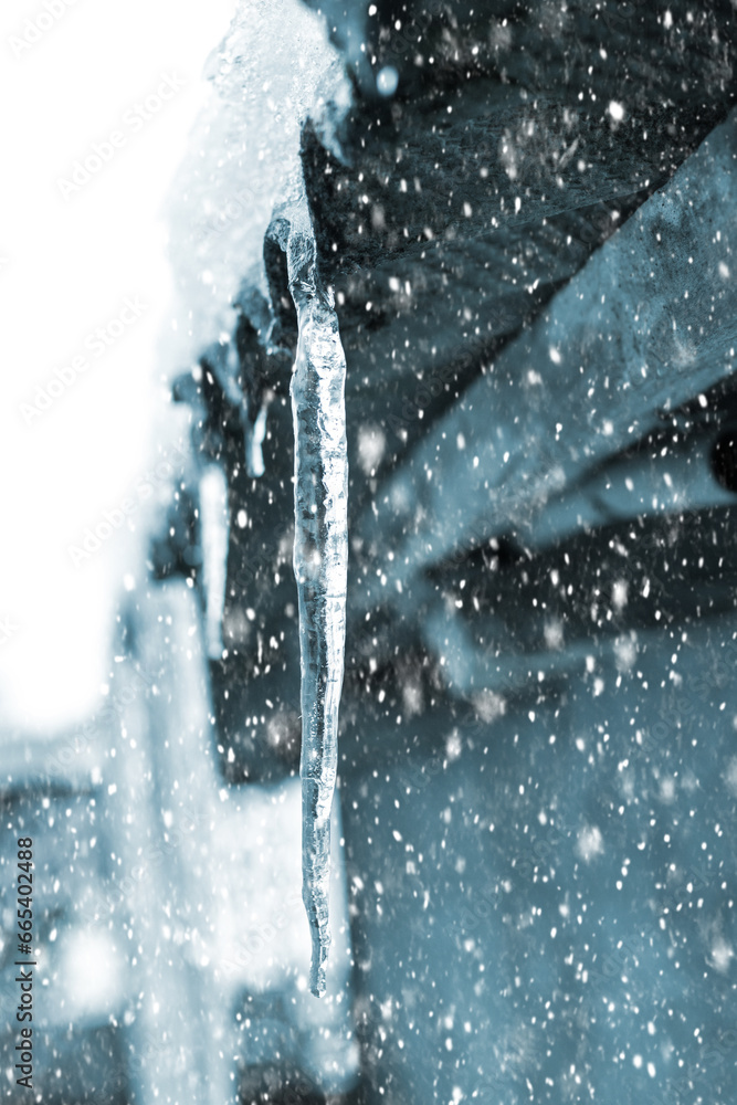 Icicles hanging from the roof of the house in winter during snowfall