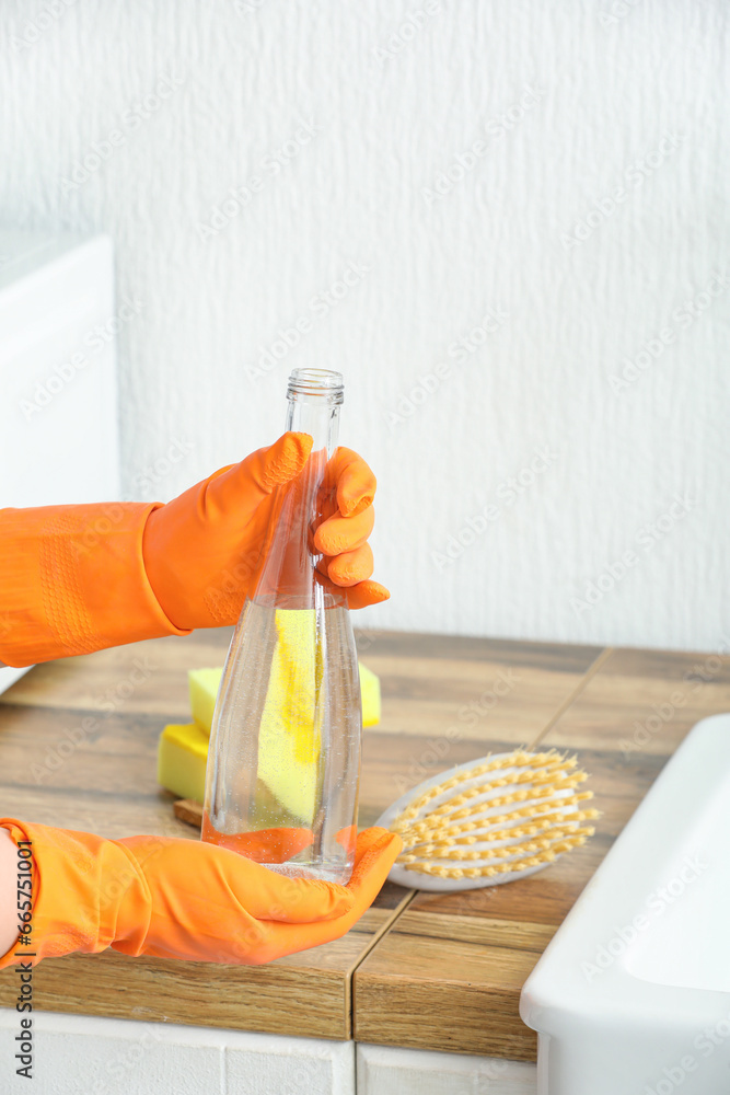 Female hands in rubber gloves with bottle of vinegar near wooden table