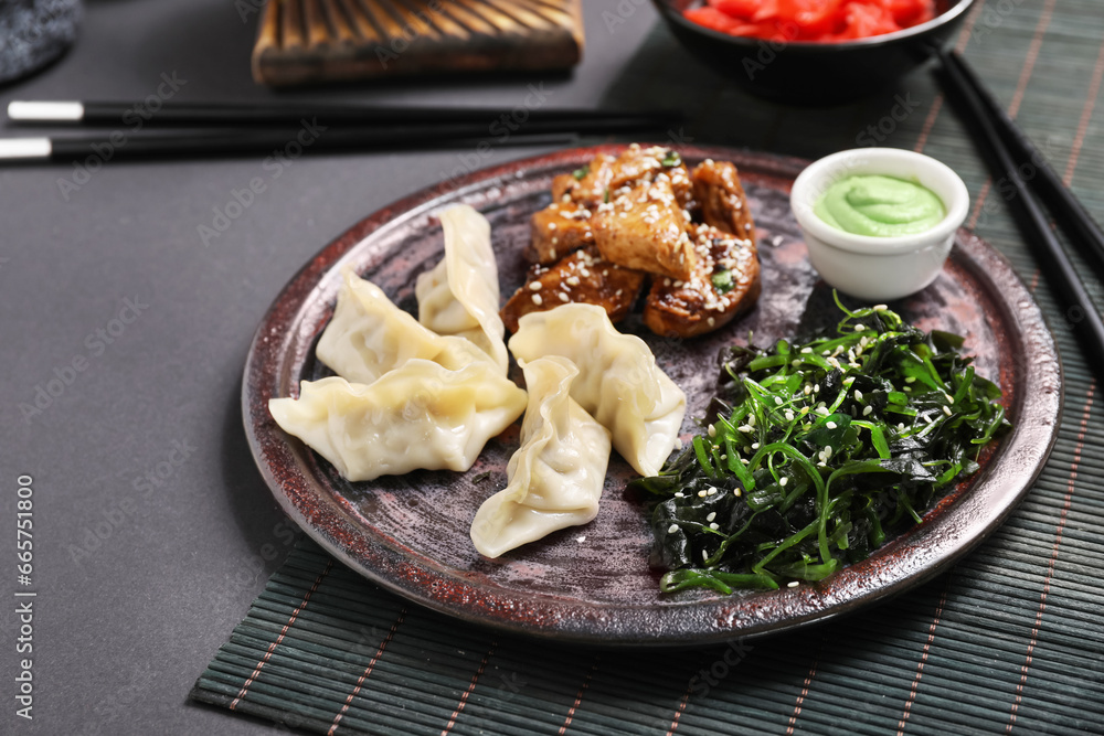 Plate with tasty Chinese dishes and chopsticks on dark background